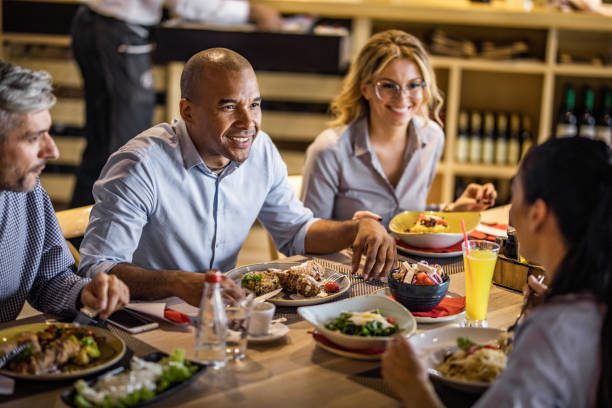 Happy black businessman communicating with his colleagues during lunch in a restaurant.